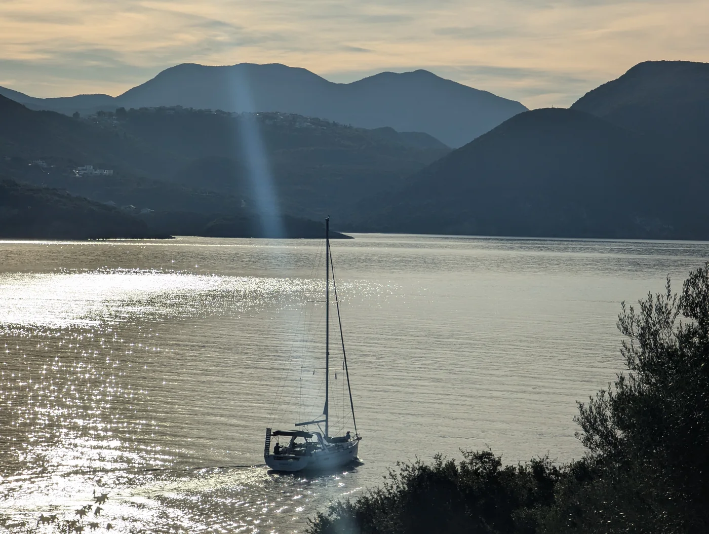 Ein Segelboot ankert im glitzernden Licht vor dunklen Bergen