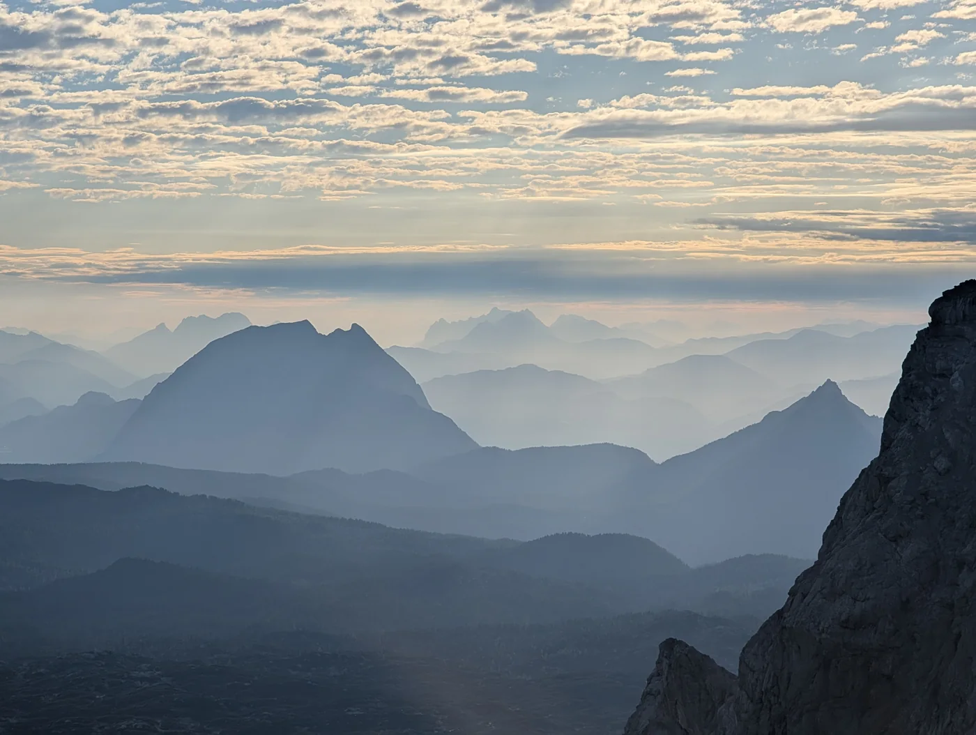 Bergketten in feinem Dunst unter einem hellen Wolkenhimmel