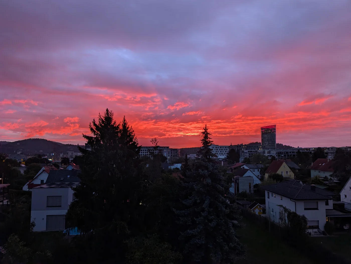 Rosa und orange Morgenwolken über Dächern und Bäumen