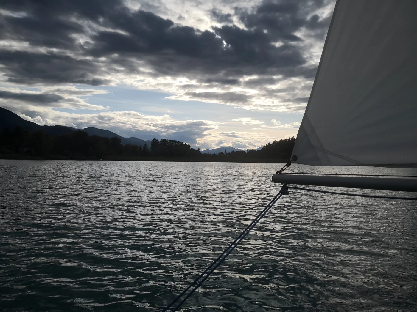 Ein weißes Segel über dunklem Wasser und weitem Wolkenhimmel