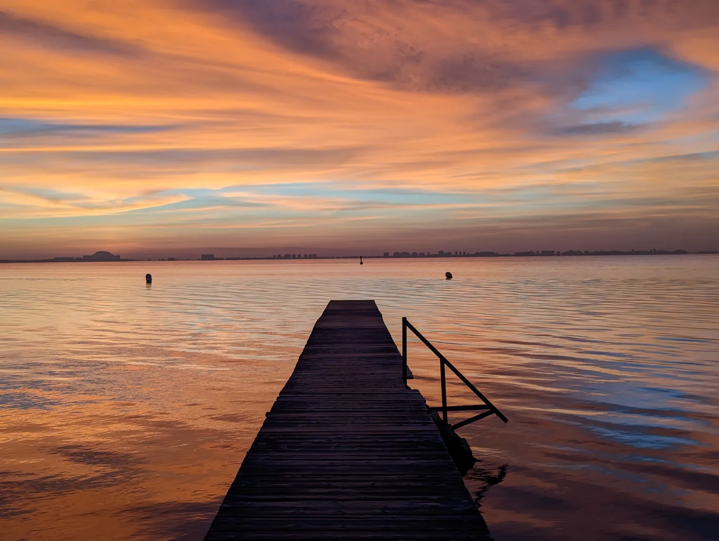 Ein Holzsteg führt in das Wasser unter einem orangefarbenen Himmel