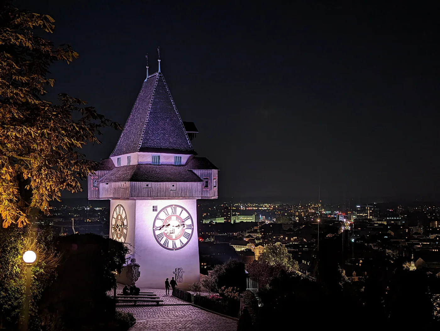 Der beleuchtete Grazer Uhrturm vor der nächtlichen Stadt