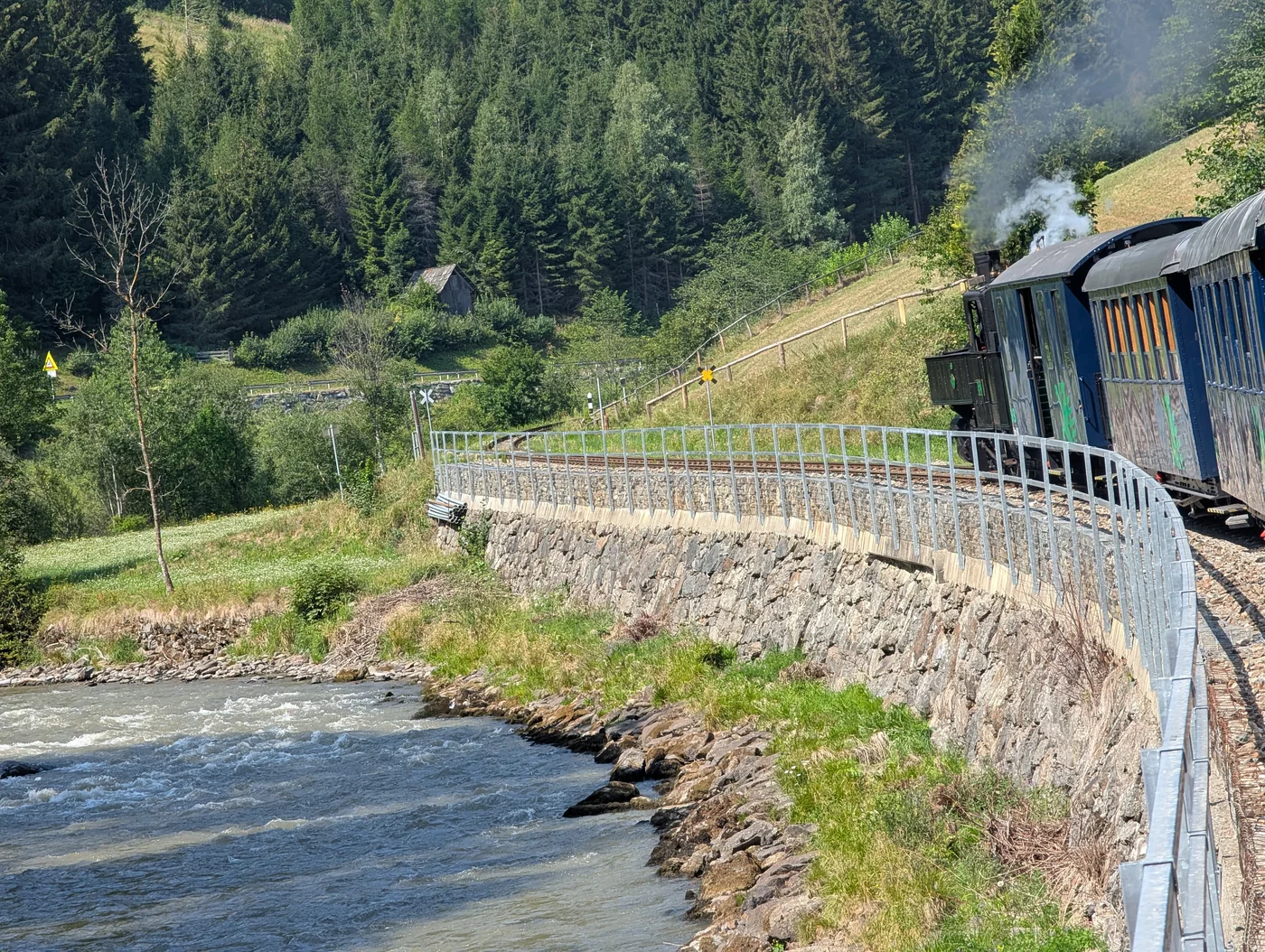 Eine Dampflokomotive fährt entlang eines Flusses durch die Berge